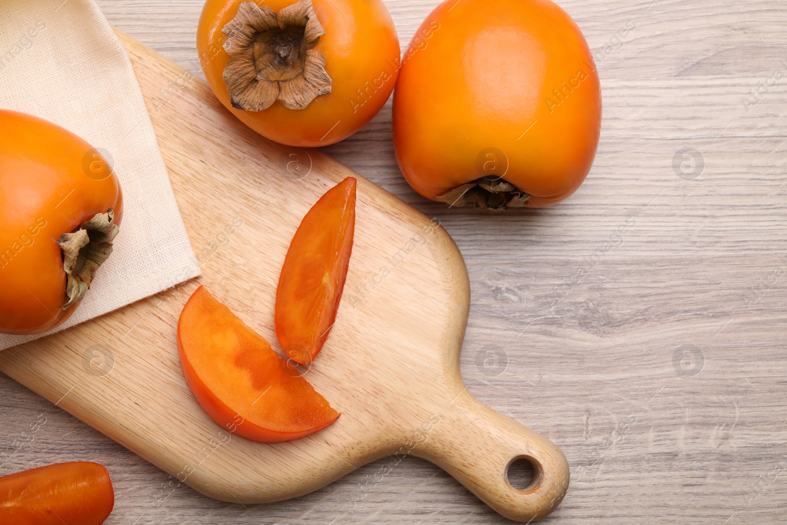 Photo of Delicious ripe persimmons on light wooden table, top view. Space for text