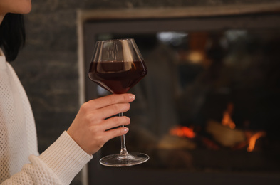 Photo of Woman with glass of wine near burning fireplace, closeup. Space for text