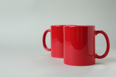 Photo of Two red ceramic mugs on light grey background. Space for text