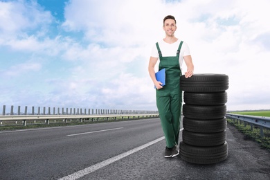 Image of Mechanic in uniform with car tires on asphalt highway outdoors, space for text