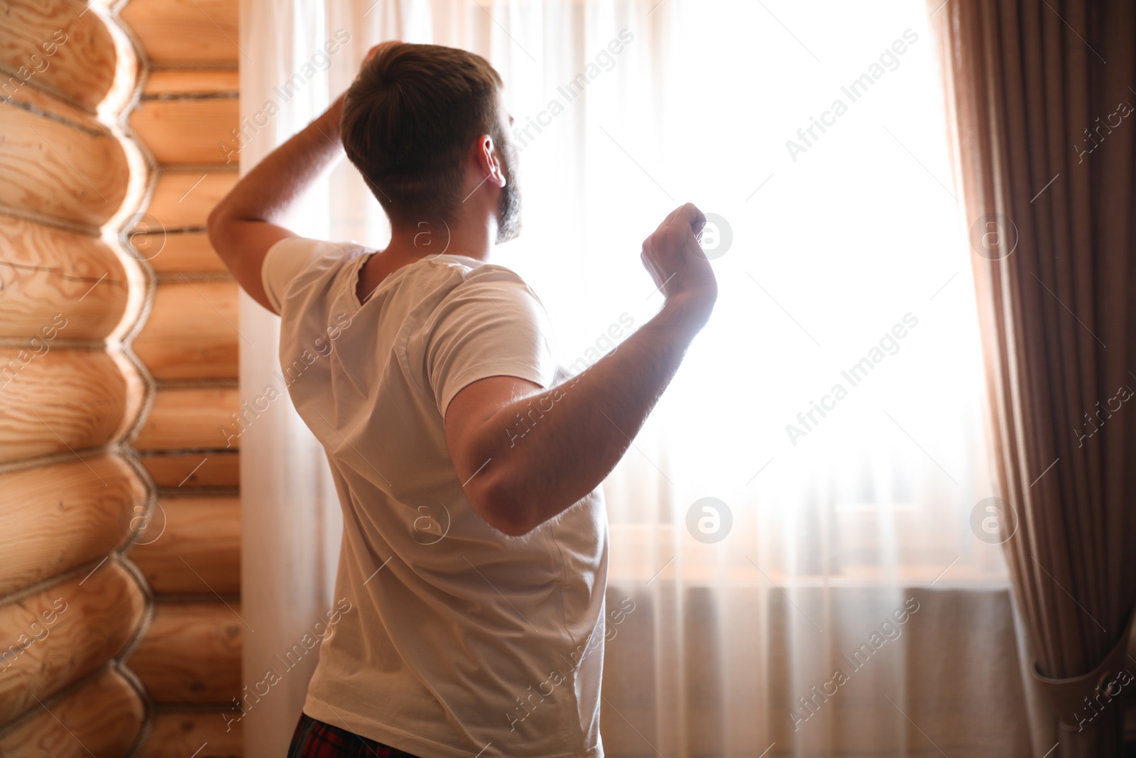 Photo of Man stretching near window indoors. Lazy morning