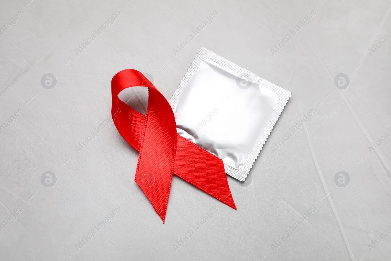 Photo of Red ribbon and condom on light grey stone background, top view. AIDS disease awareness