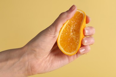 Photo of Woman squeezing juicy orange on beige background, closeup