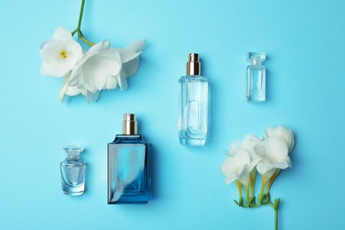 Photo of Bottles of perfume and flowers on color background, top view