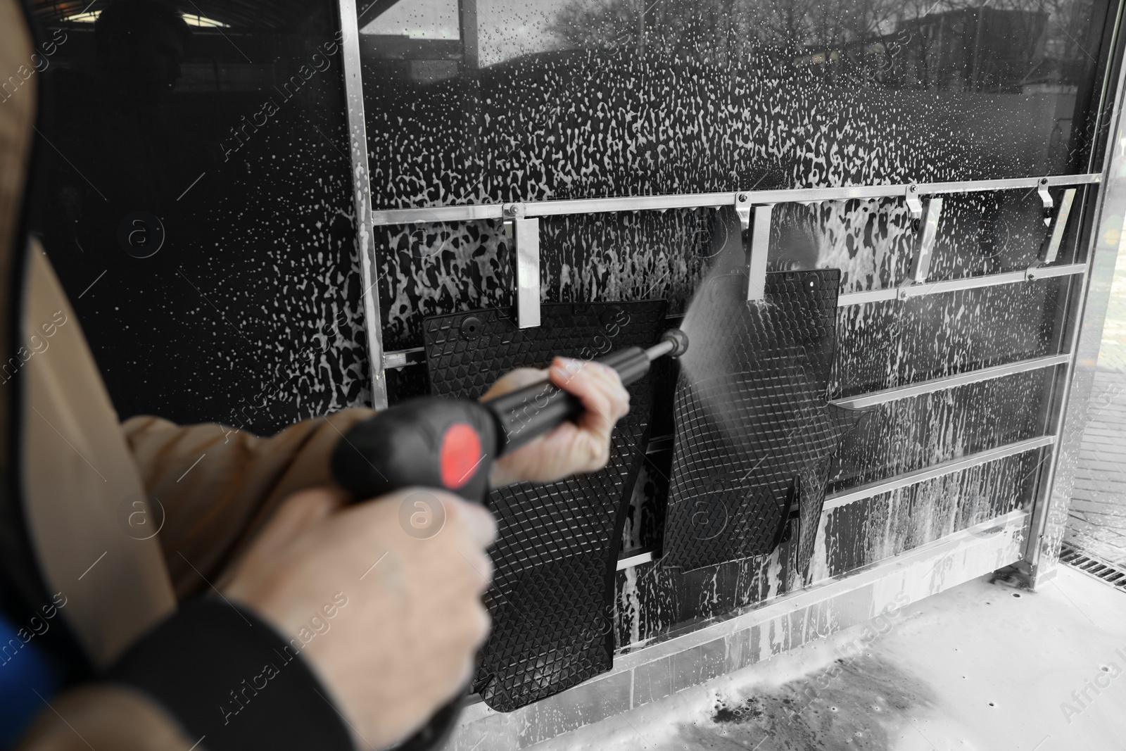 Photo of Man cleaning auto mats with high pressure water jet at self-service car wash, closeup