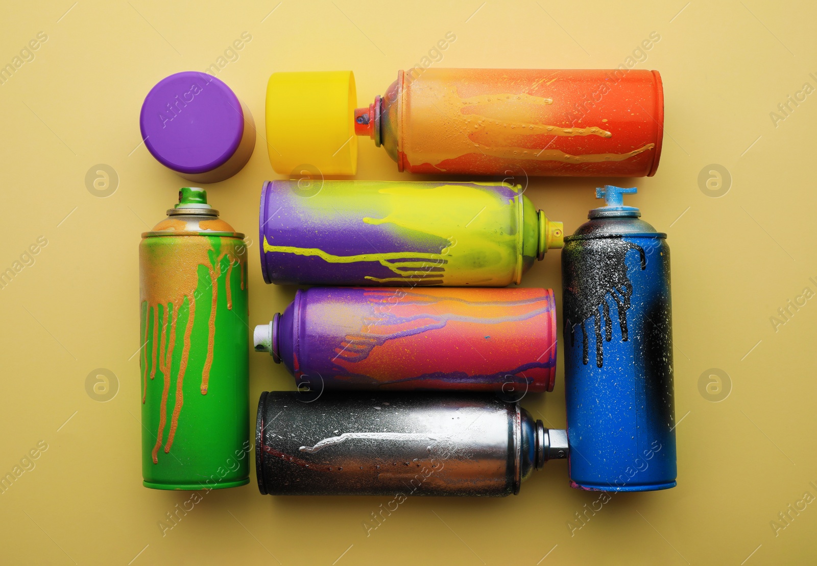 Photo of Used cans of spray paints on beige background, flat lay. Graffiti supplies