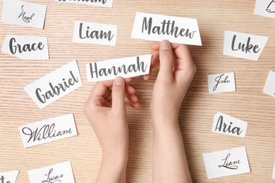 Photo of Woman choosing baby name at wooden table, top view