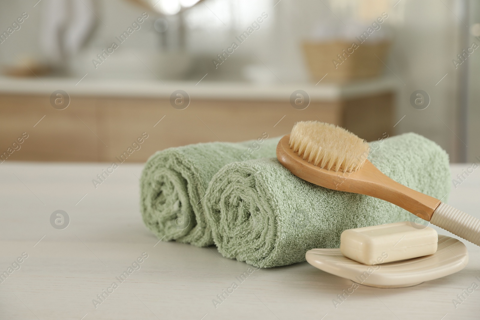 Photo of Clean rolled towels, massage brush and bar of soap on table in bathroom