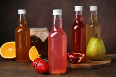 Photo of Delicious kombucha in glass bottles, jar and fresh fruits on wooden table