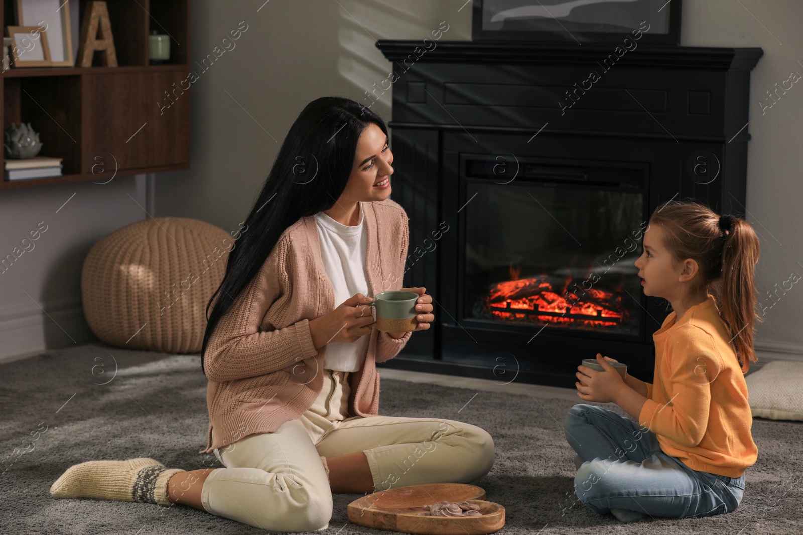 Photo of Happy mother and daughter spending time together on floor near fireplace at home