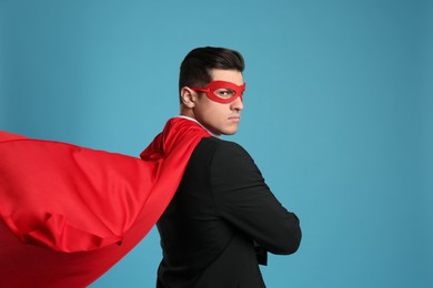 Man wearing superhero cape and mask on light blue background