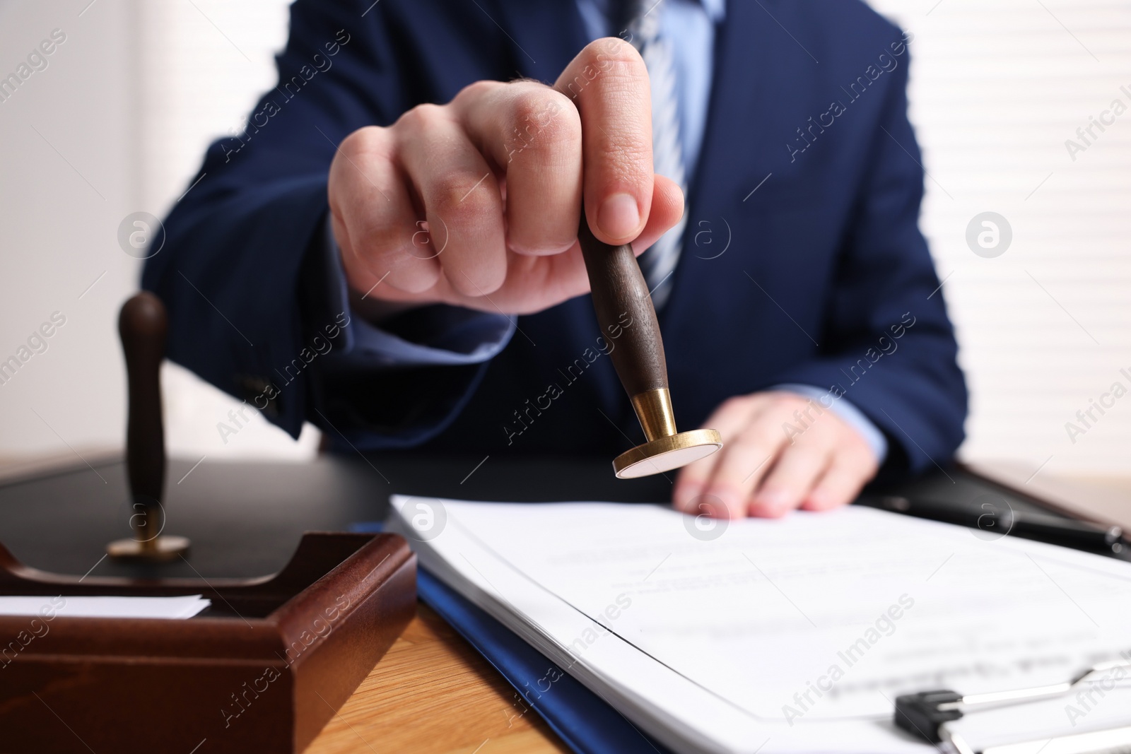 Photo of Notary stamping document at wooden table in office, closeup