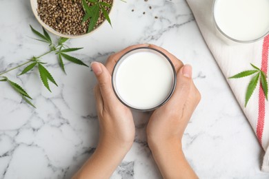 Woman with hemp seed milk at white marble table, top view