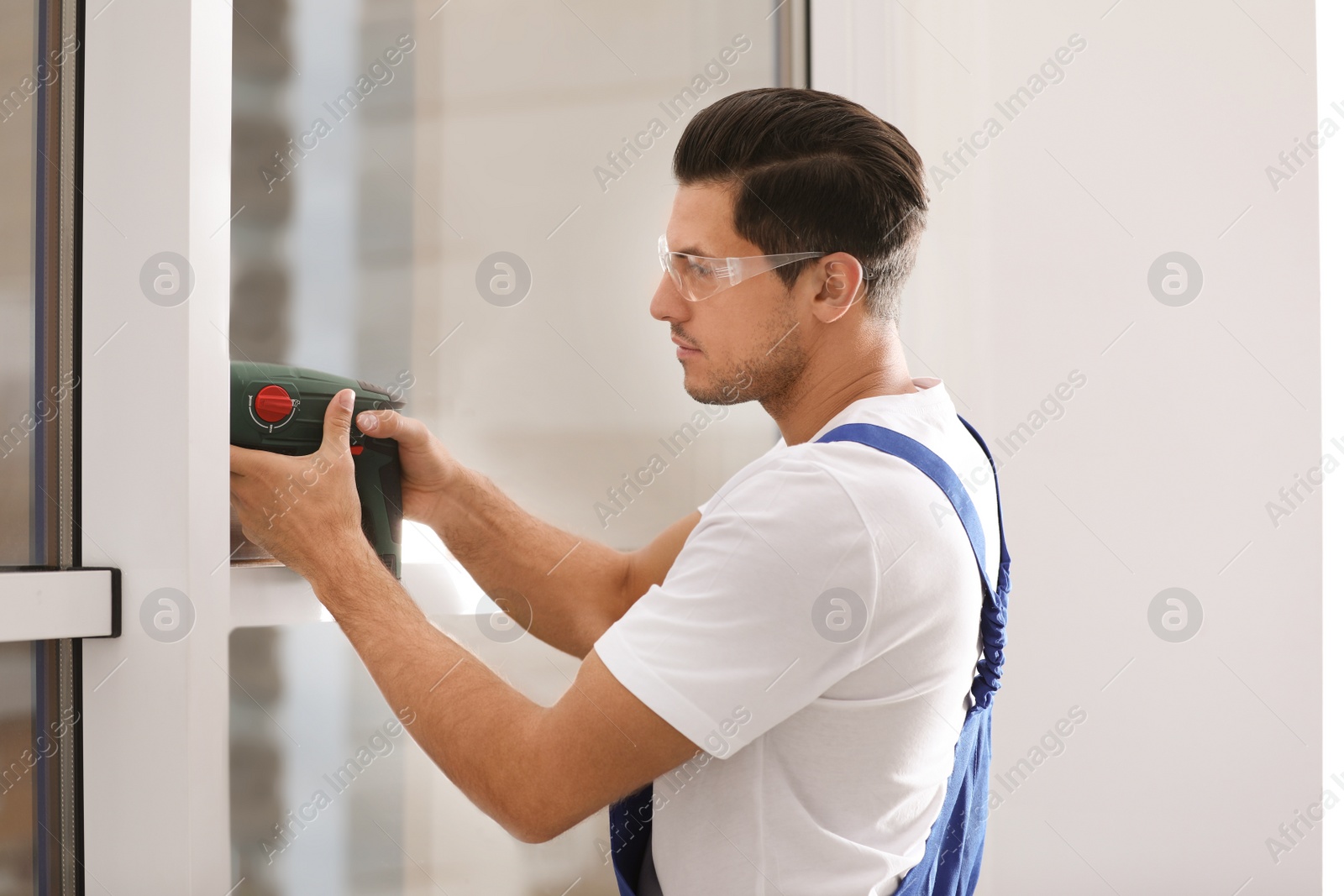 Photo of Construction worker repairing plastic window with electric screwdriver indoors