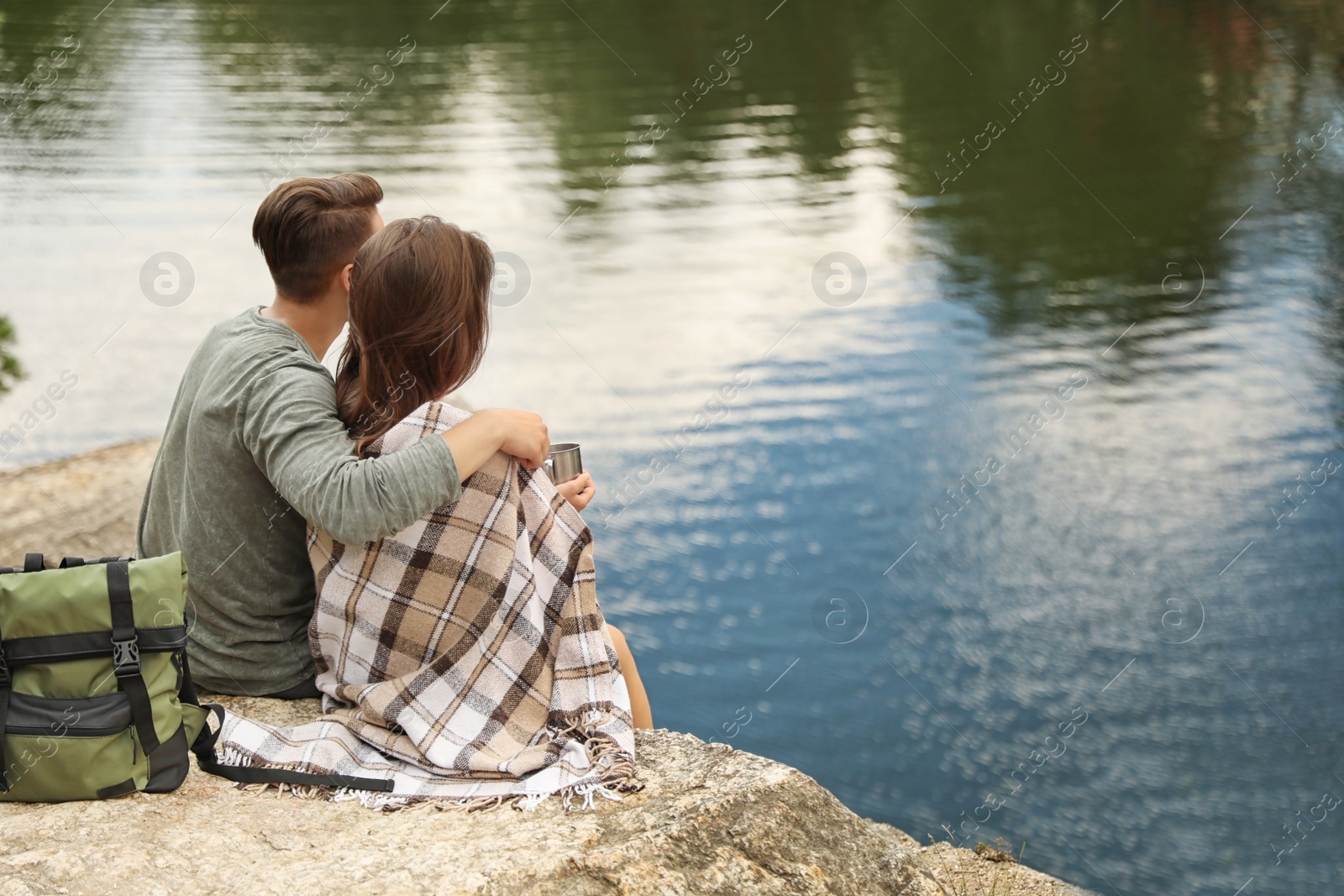 Photo of Cute couple with mugs and plaid near lake. Camping season