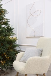 Stylish armchair near beautiful Christmas tree decorated with festive lights indoors