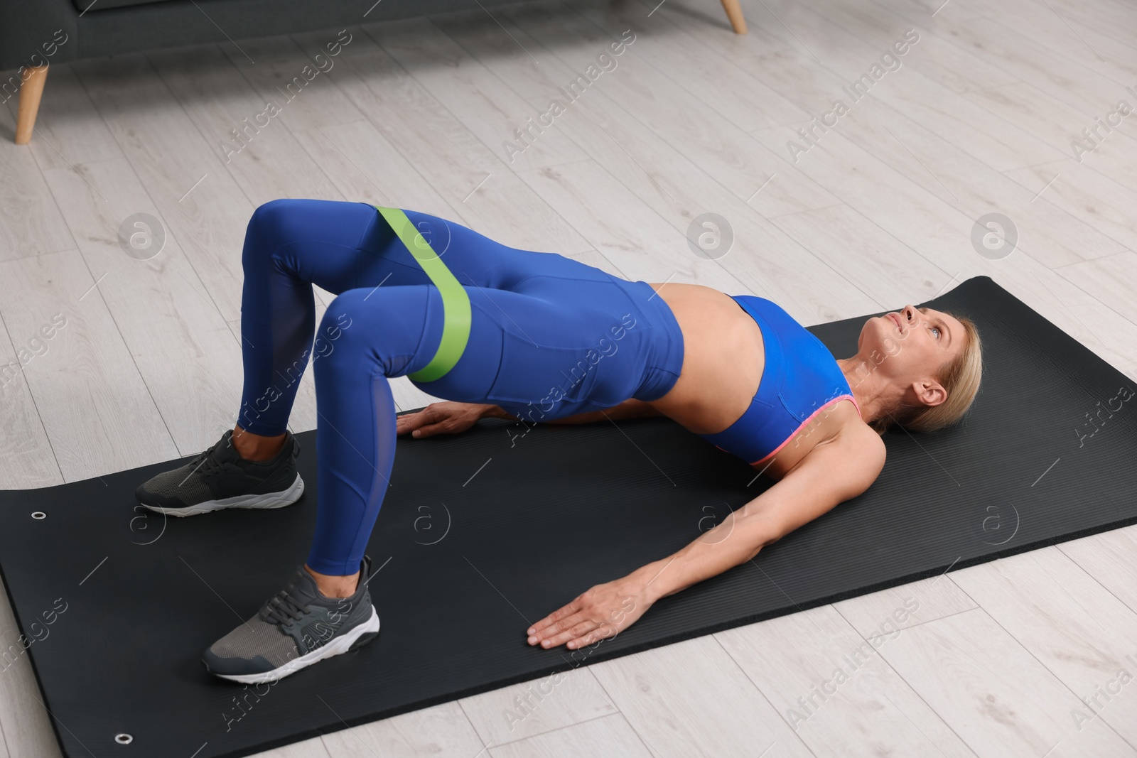 Photo of Athletic woman doing exercise with fitness elastic band on mat indoors