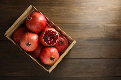 Ripe pomegranates in crate on wooden table, top view. Space for text