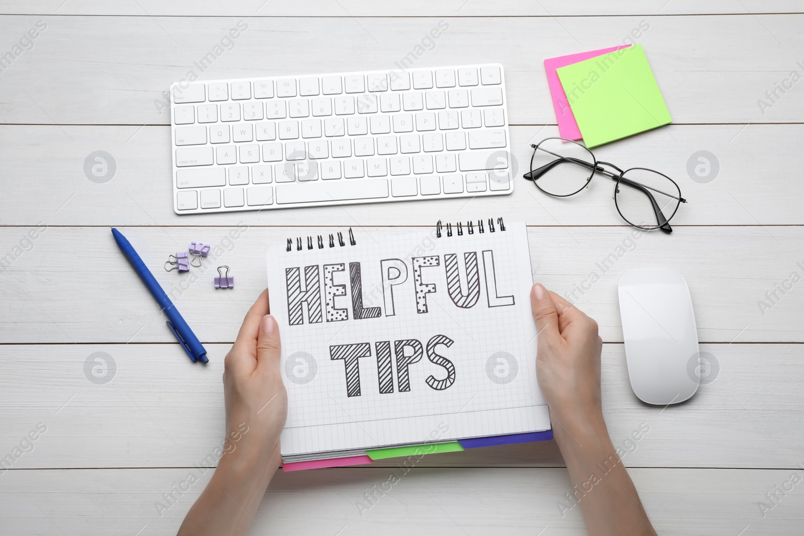 Photo of Woman holding notebook with phrase Helpful Tips at white wooden table, top view