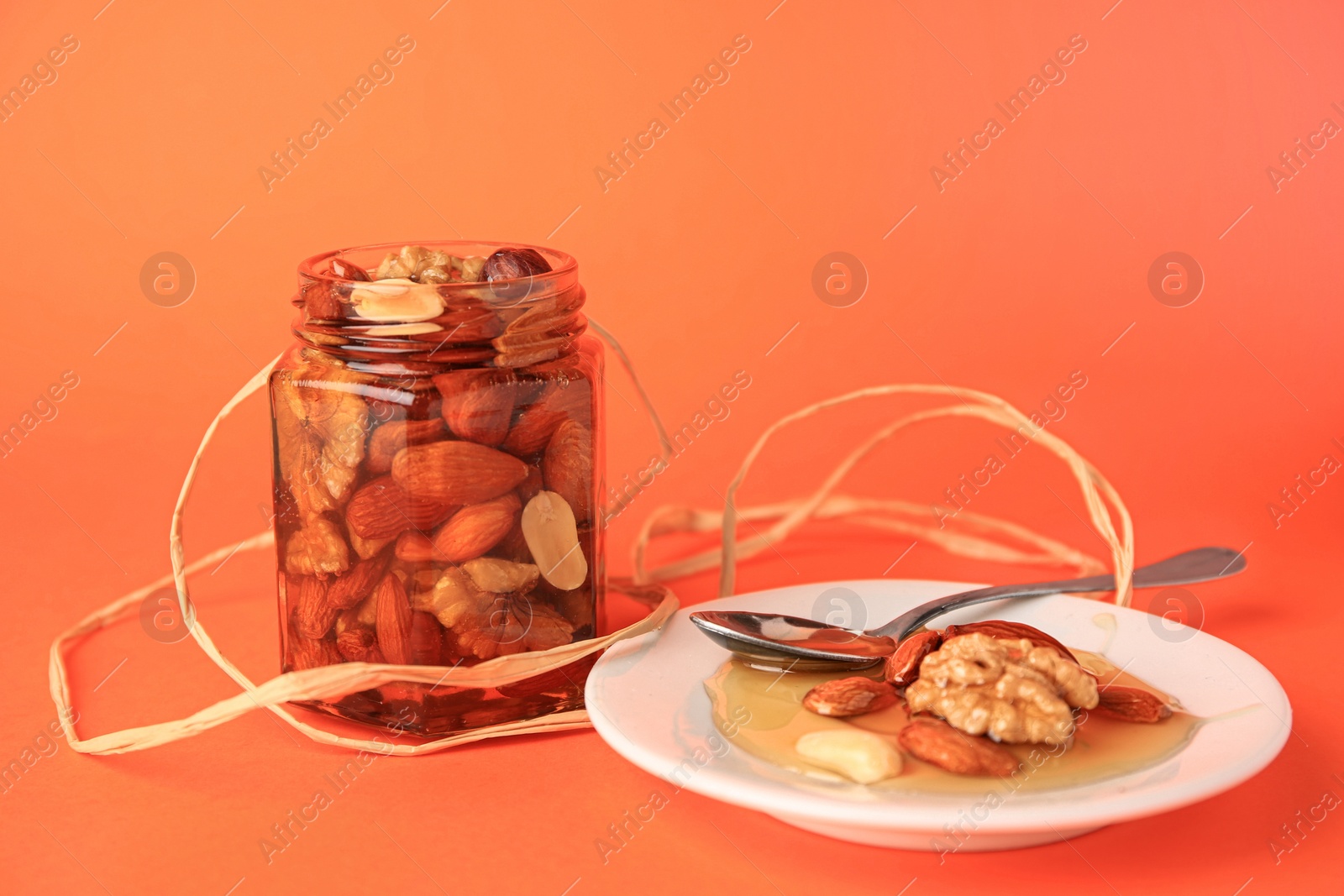 Photo of Different tasty nuts with honey on orange background