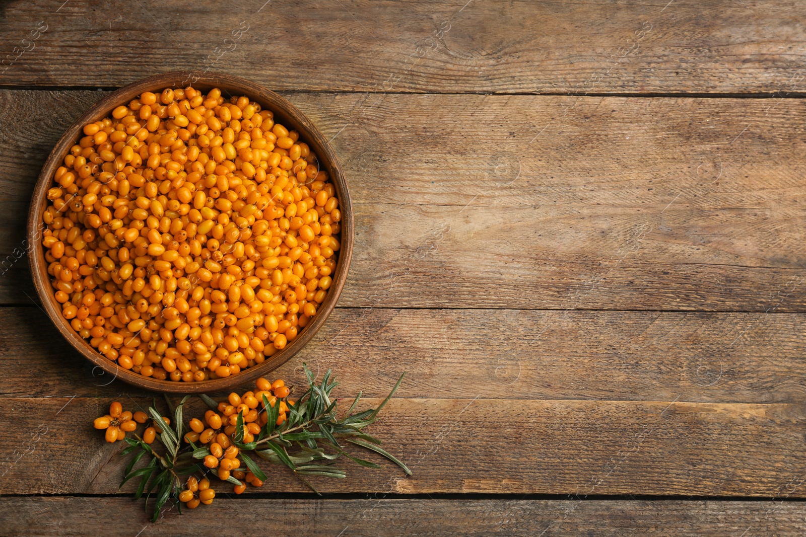 Photo of Ripe sea buckthorn berries on wooden table, flat lay. Space for text