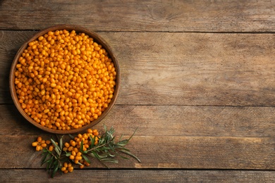 Photo of Ripe sea buckthorn berries on wooden table, flat lay. Space for text