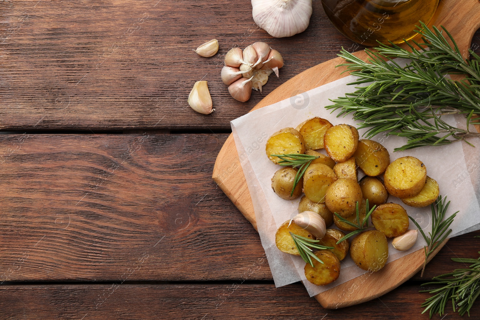 Photo of Delicious baked potatoes with rosemary and garlic on wooden table, flat lay. Space for text