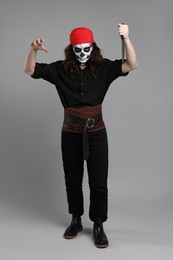 Man in scary pirate costume with skull makeup and knife on light grey background. Halloween celebration