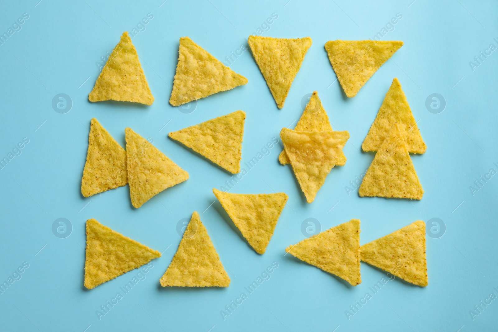 Photo of Flat lay composition of tasty tortilla chips (nachos) on light blue background