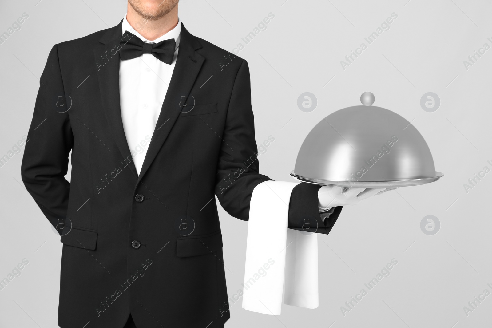 Photo of Waiter holding metal tray with lid on light background