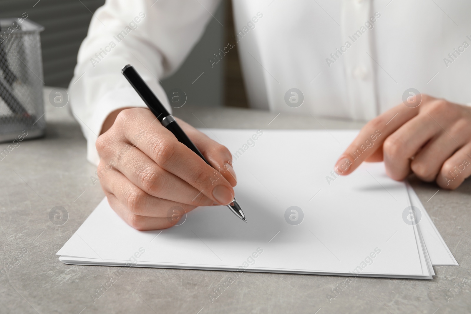 Photo of Woman with pen and paper sheets at grey table, closeup