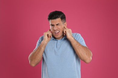 Photo of Emotional man covering ears with fingers on pink background