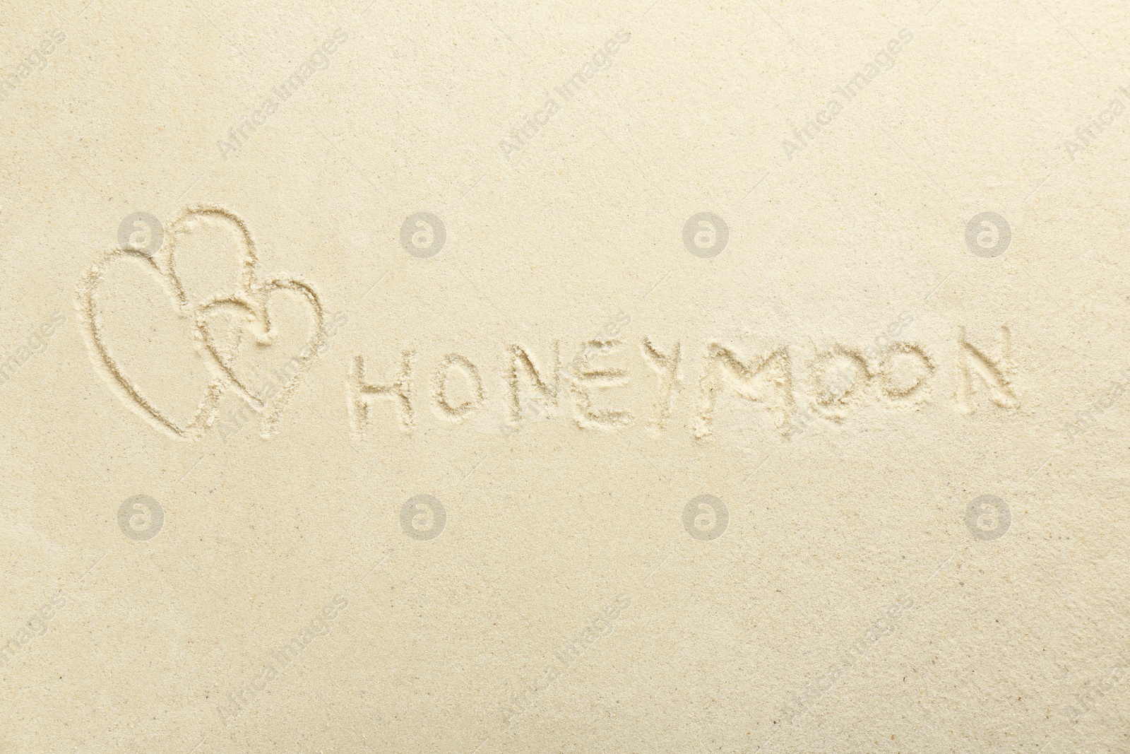 Photo of Word Honeymoon written on sand and hearts, top view