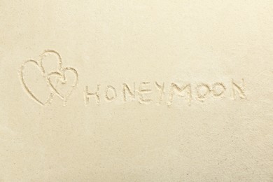 Word Honeymoon written on sand and hearts, top view