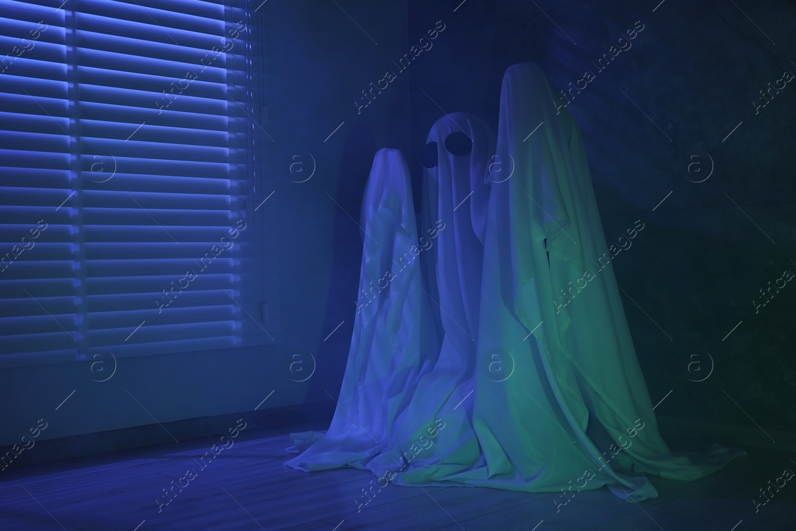 Photo of Creepy ghost. Woman covered with sheet near window in blue light