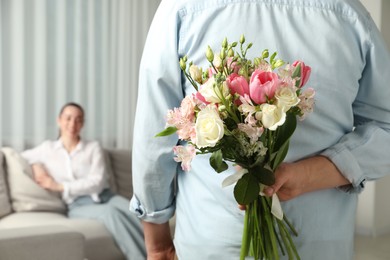 Man hiding bouquet of flowers for his beloved woman indoors, closeup