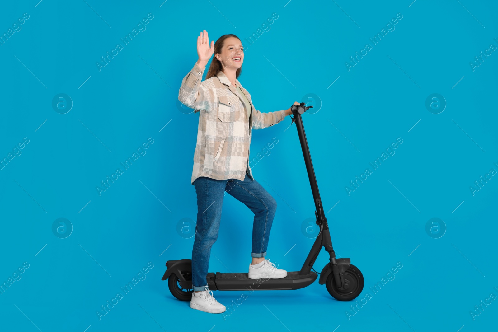 Photo of Happy woman with modern electric kick scooter on light blue background