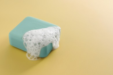 Photo of Soap bar with fluffy foam on yellow background, space for text