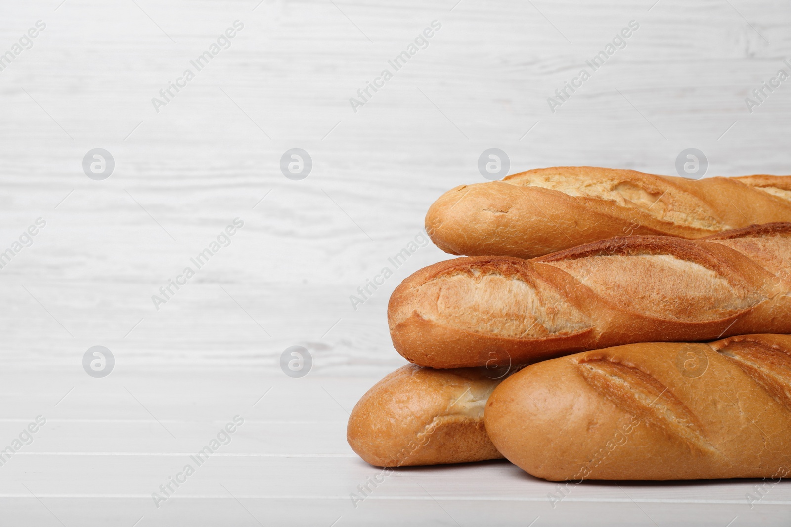 Photo of Tasty baguettes on white wooden table. Space for text