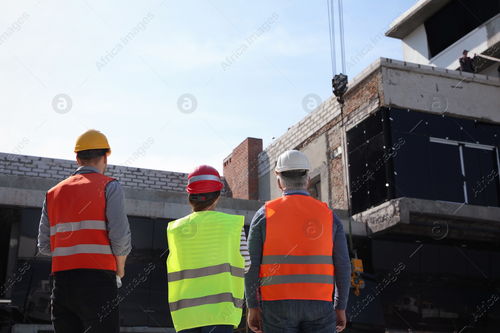 Photo of Professional engineers in safety equipment at construction site, back view
