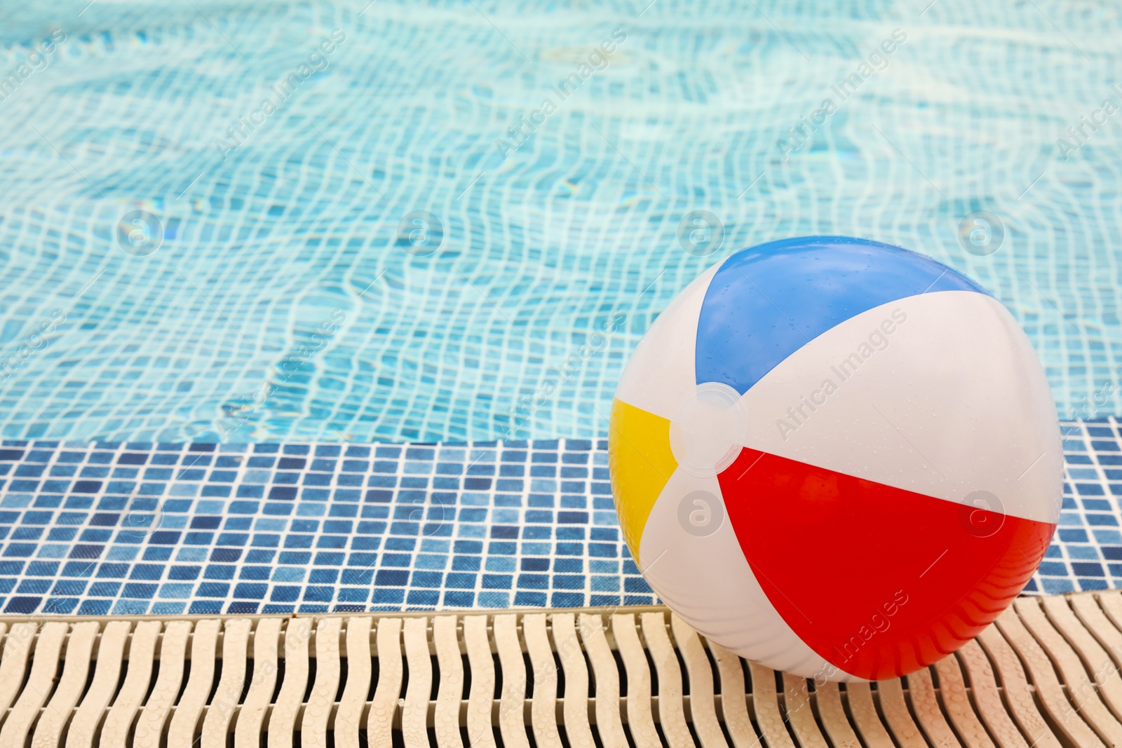 Photo of Inflatable colorful beach ball on edge of outdoor swimming pool, space for text