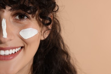 Photo of Beautiful young woman with sun protection cream on her face against beige background, closeup. Space for text