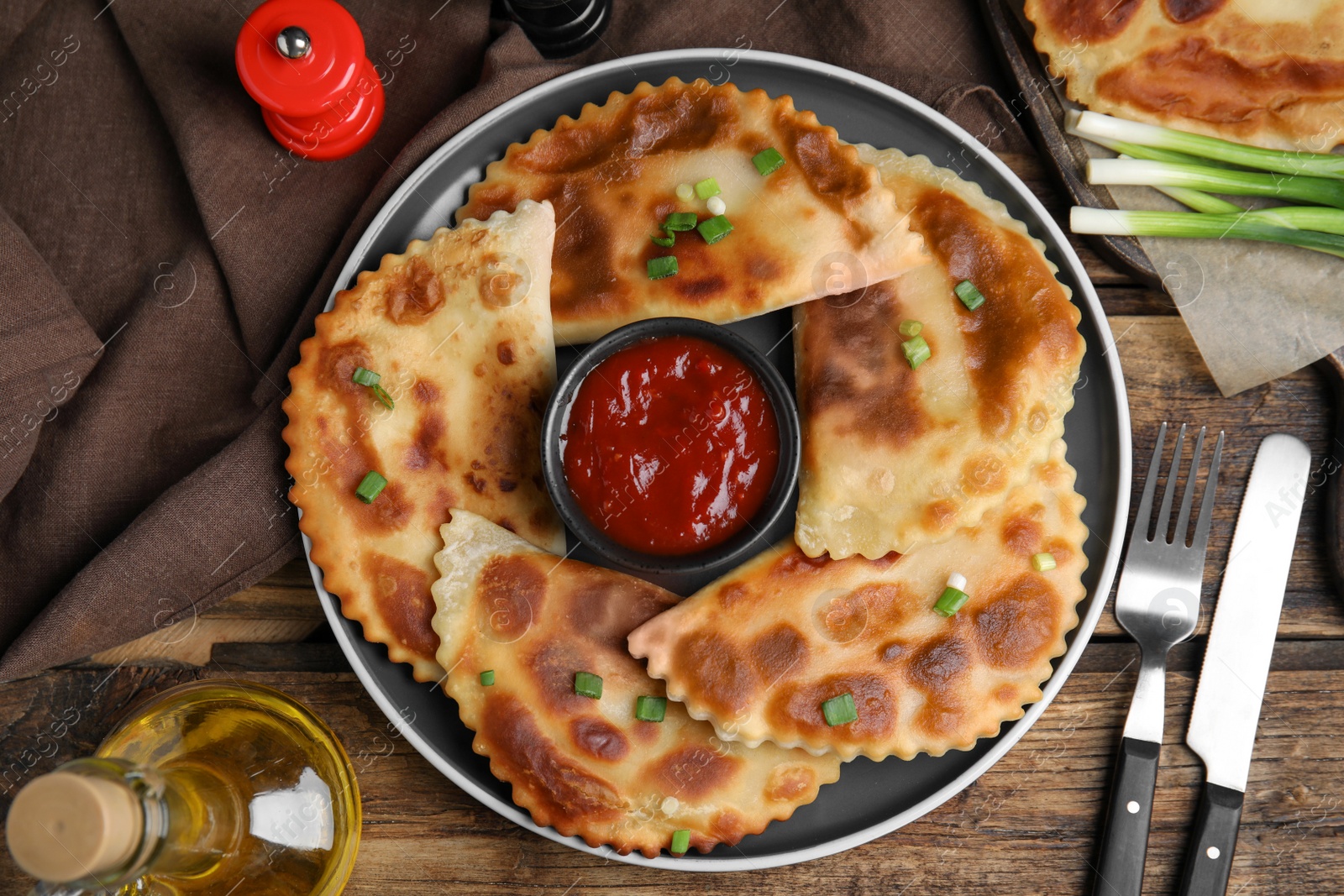 Photo of Delicious fried chebureki with ketchup served on wooden table, flat lay