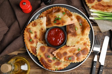 Photo of Delicious fried chebureki with ketchup served on wooden table, flat lay