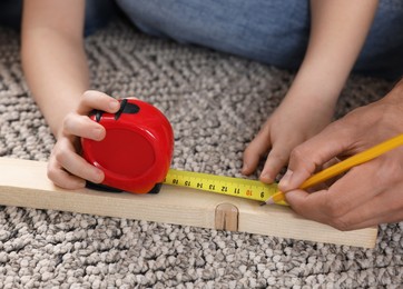 Photo of Father and son measuring plank on rug, closeup. Repair work