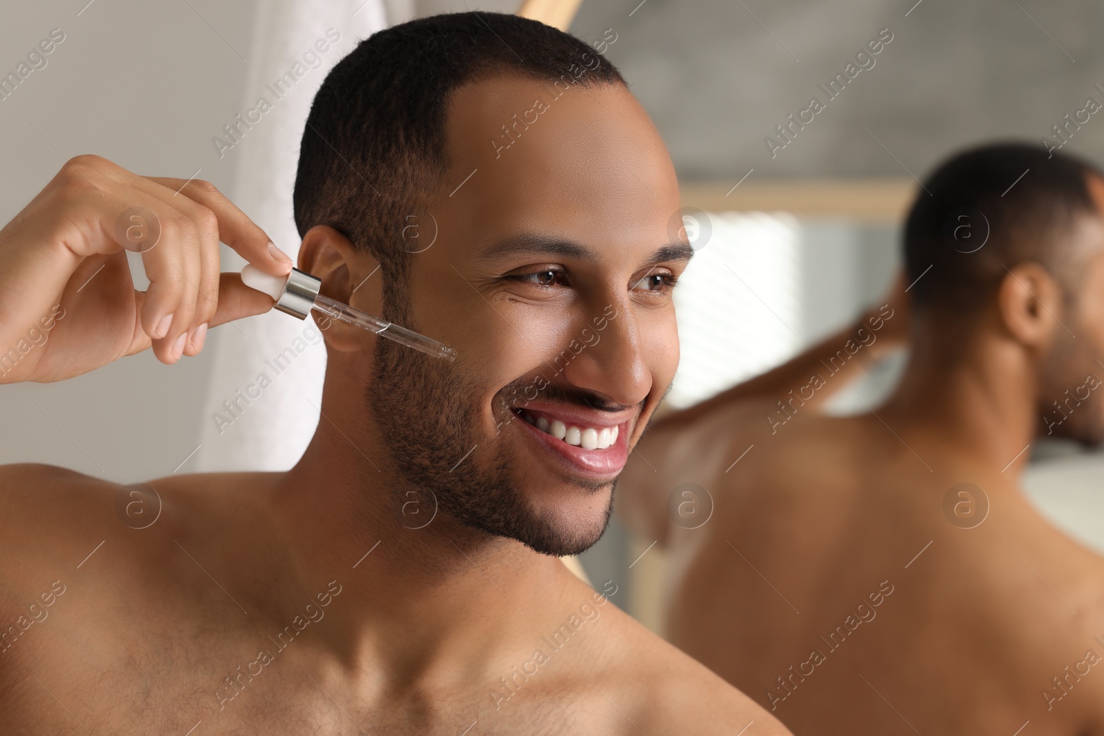 Photo of Handsome man applying cosmetic serum onto face in bathroom, space for text