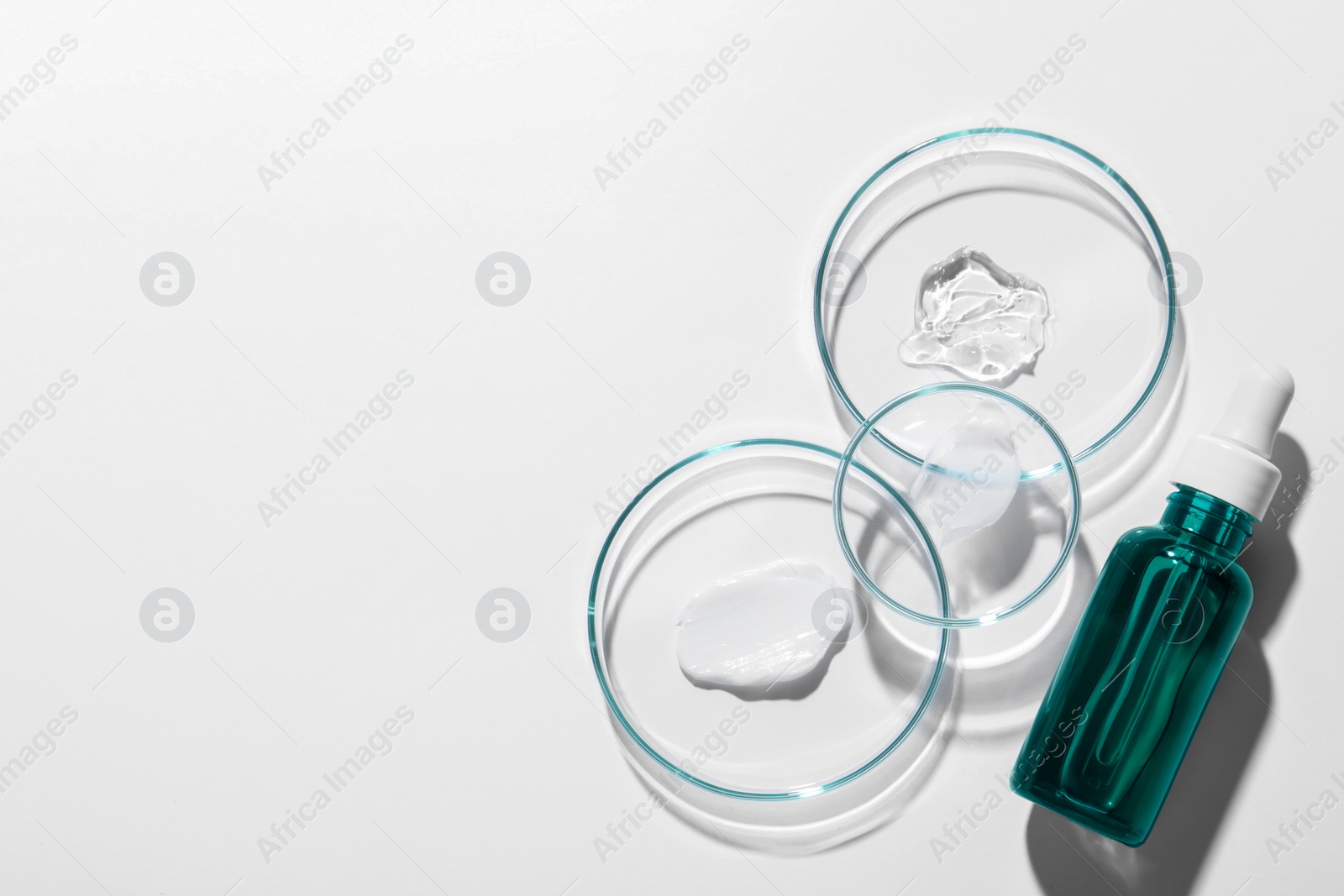 Photo of Bottle of cosmetic serum and petri dishes with samples on white background, flat lay. Space for text