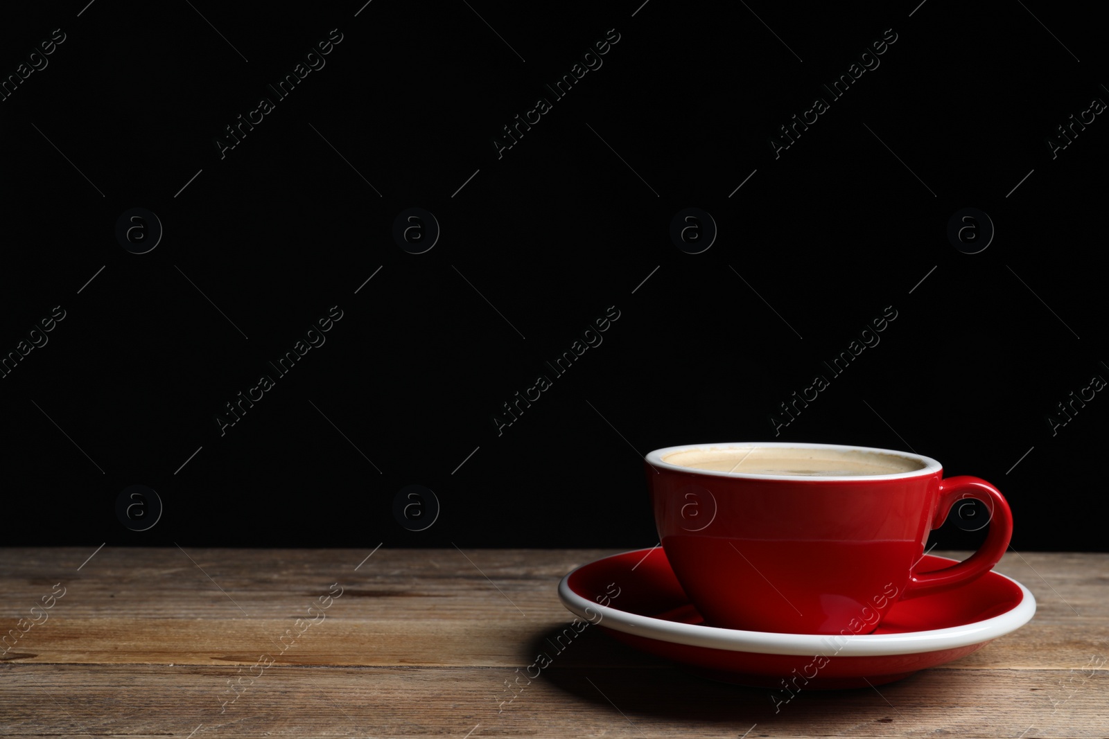 Photo of Red ceramic cup with hot aromatic coffee on wooden table against black background, space for text