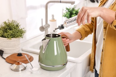 Woman pouring vinegar from bottle into electric kettle in kitchen, closeup