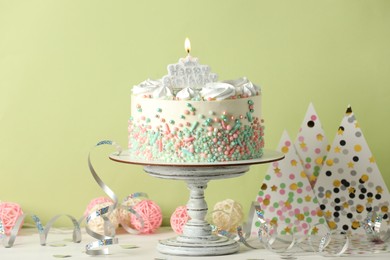 Photo of Delicious birthday cake and party decor on white wooden table against light background